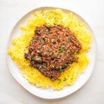 White rimmed plate filled with spaghetti squash and covered with red lentil vegan bolognese sauce.