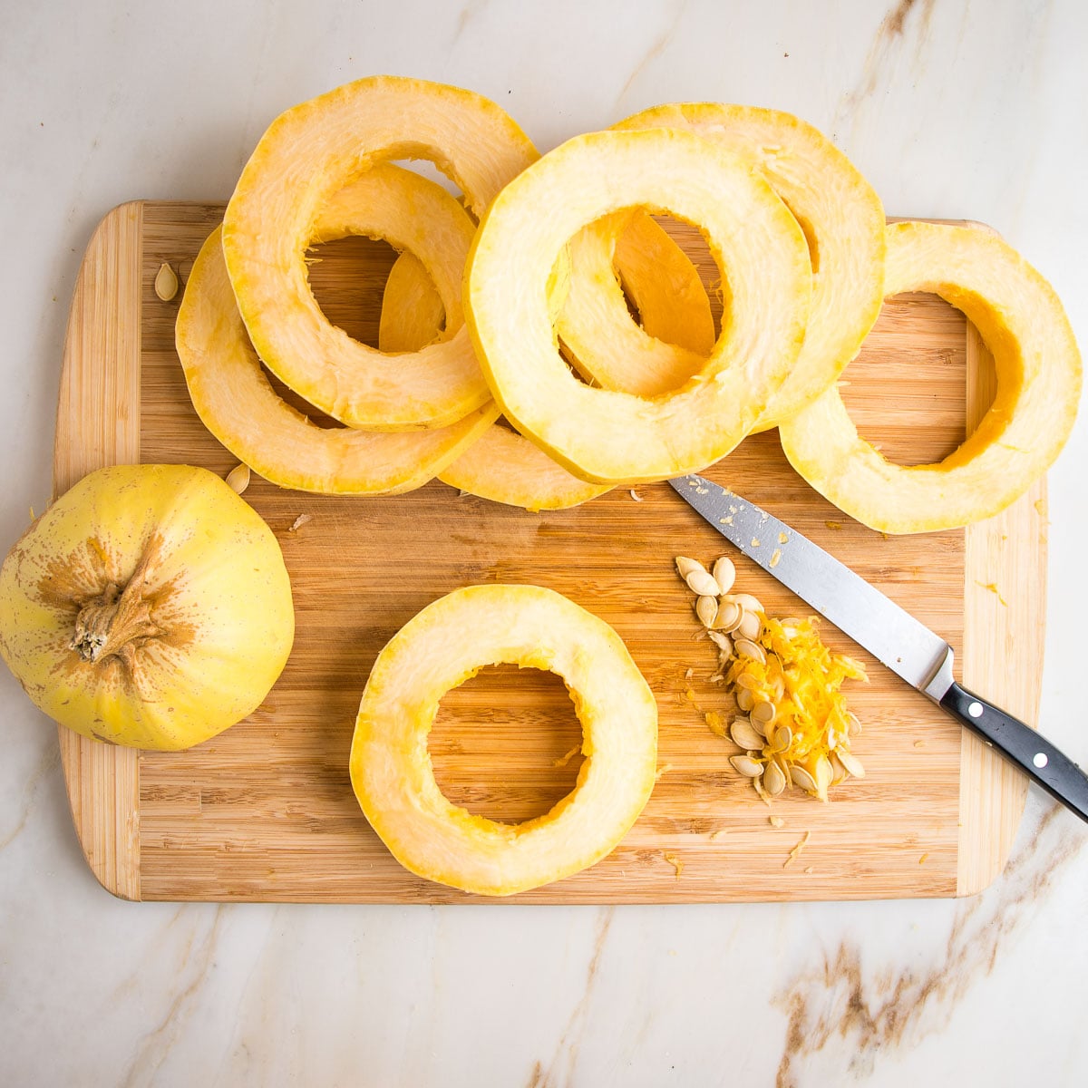 Using a sharp knife to cut out the stringy center and seeds from a ring of spaghetti squash.