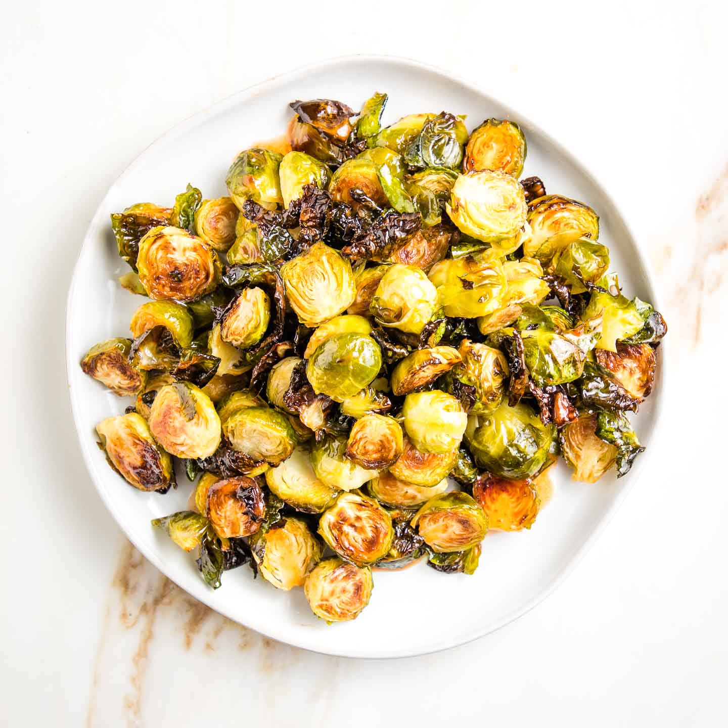 Round plate filled with roasted brussels sprouts with sweet and spicy drizzle