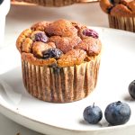 Blueberry muffin with a couple blueberries on the plate.