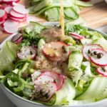 Dressing poured over a crisp green salad with radish, cucumber and capers.