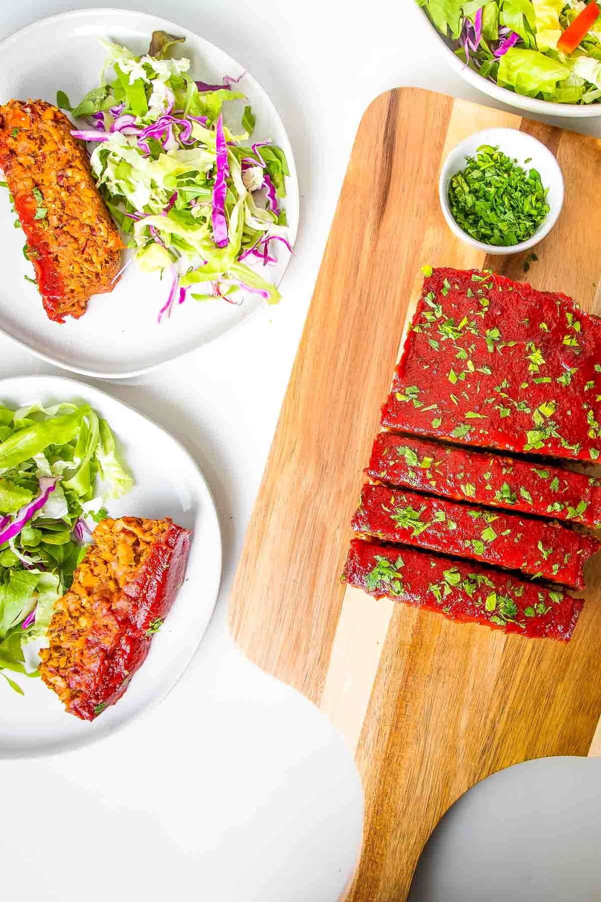 Sliced meatloaf on a cutting board. Plates with meatloaf and a side salad.