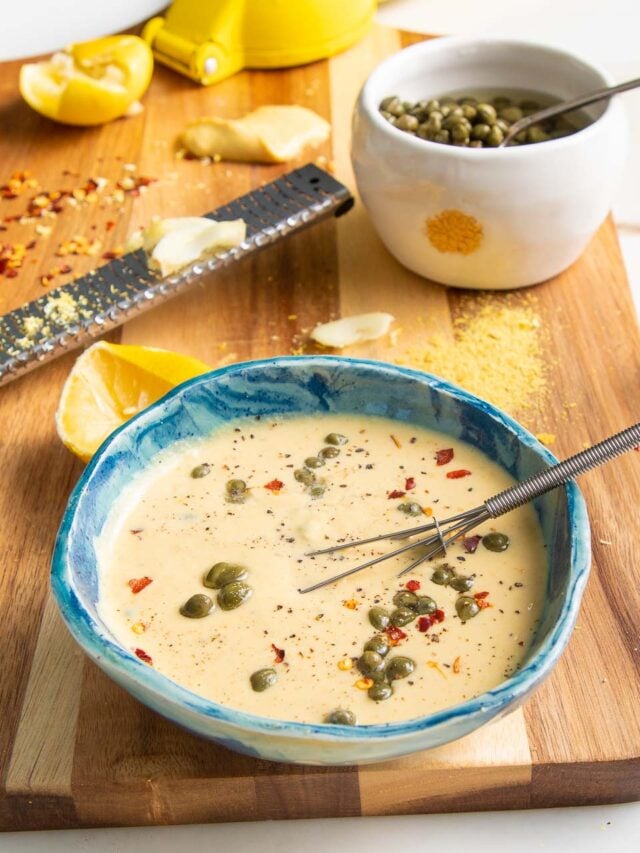 Whisking a small bowl of caesar dressing with capers, lemon and crushed red pepper.