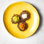 Three latkes with different toppings: applesauce, guacamole and sour cream.