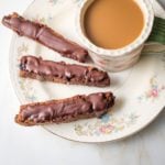 flowery china plate with three chocolate covered biscotti and a cup of coffee