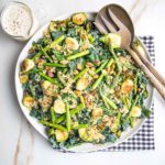 White plate with greens, veggies, crispy quinoa and a creamy dressing.