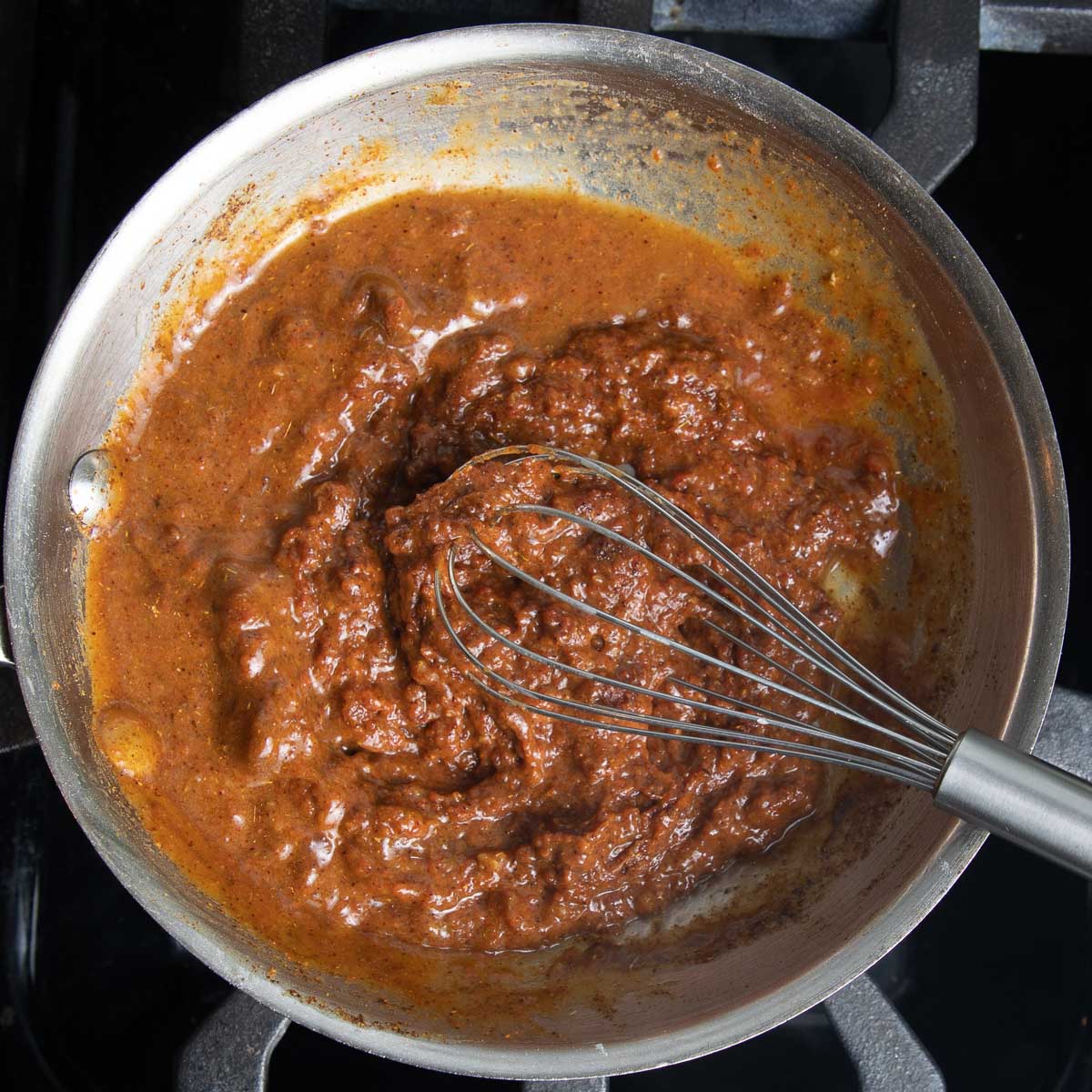 Thick and pasty enchilada sauce being whisked in a skillet to thin it out.