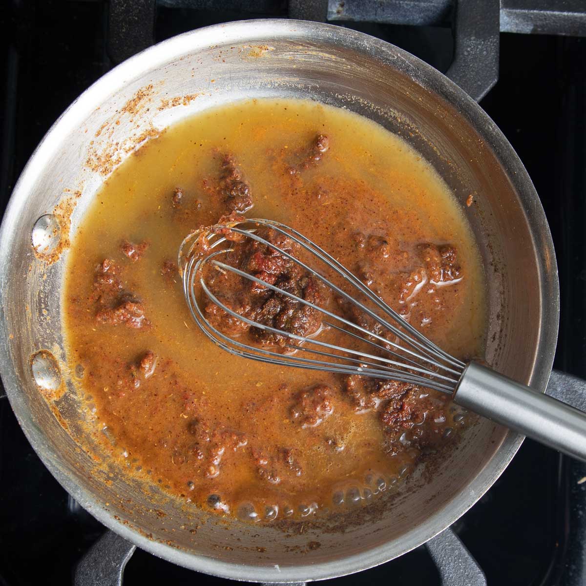 Using veggie stock and a whisk to thin out a pasty roux with endhilada spices.