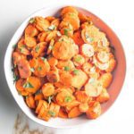 white bowl filed with spiced carrot rounds, sprinkled with chopped green parsley