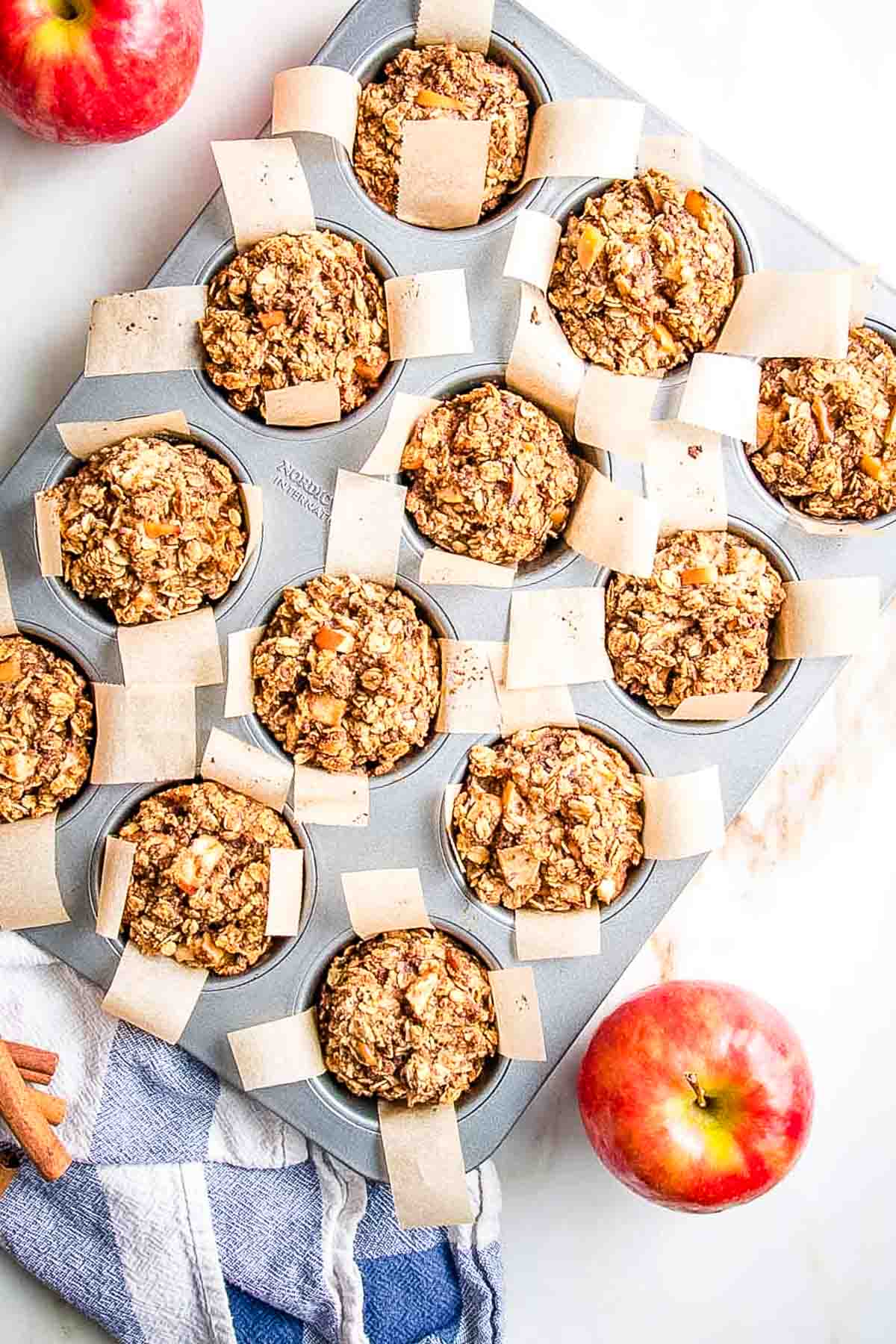 Chunks of apples in oatmeal muffins lined with parchment in muffin tins.