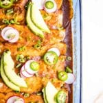 Casserole Dish with enchiladas, garnished with avocado slices, jalapenos and radishes.