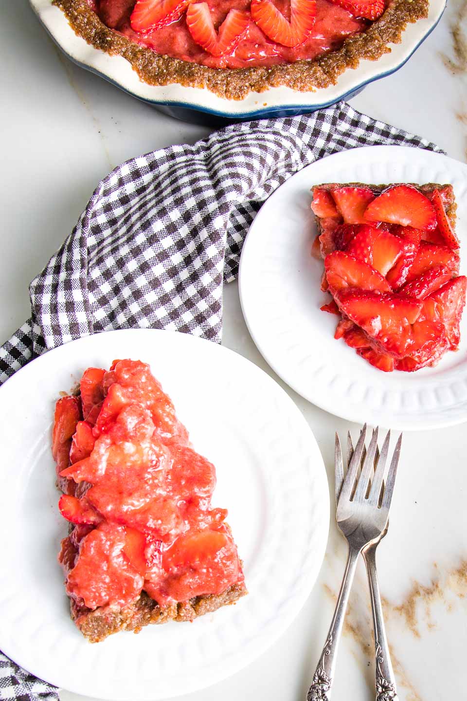 Slices of raw strawberry pie on plates near the whole pie.
