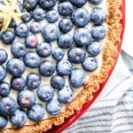 Right corner close up of blueberry tart with creamy filling on a bright red cake stand.