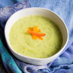 Light green creamy soup with red pepper slices as garnish.