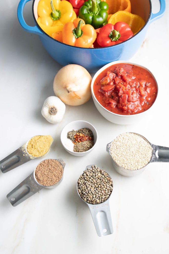 Ingredients for vegan stuffed peppers: colorful bell peppers, diced tomatoes, quinoa, lentils, onions, garlic, Italian spices, ground flax and nutritional yeast.