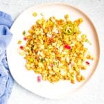 Mexican Street Corn Salad with red onions, jalapenos, cilantro and spices on a large white rimmed plate atop a blue napkin