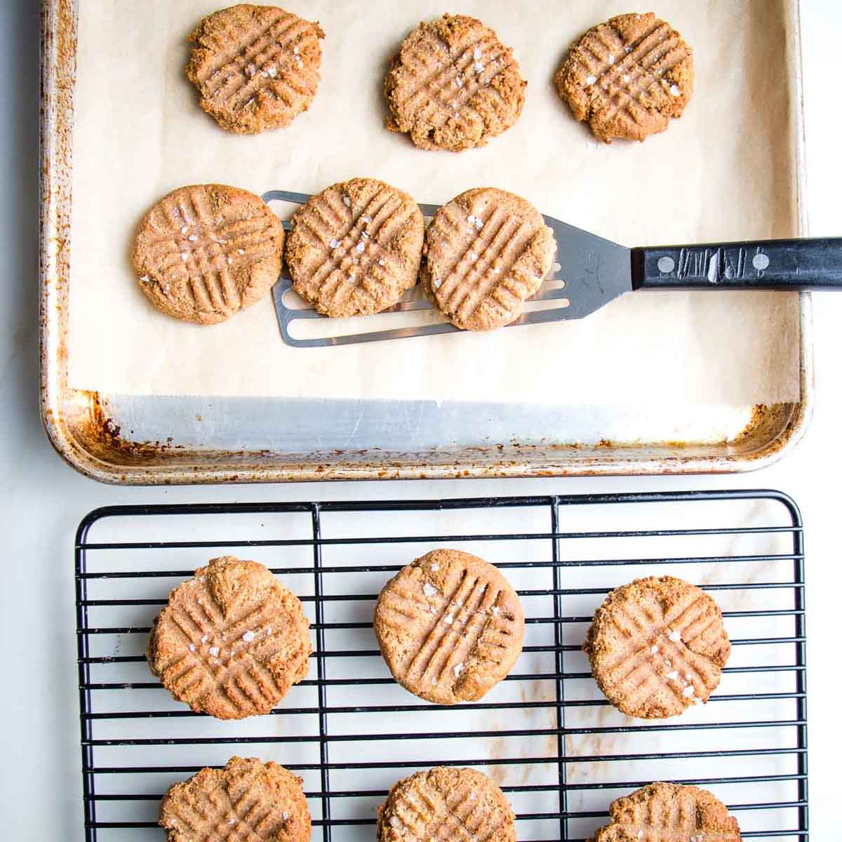Spatula removing peanut butter cookies off a baking tray and onto a wire rack. 