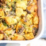 White casserole dish filled with vegan cornbread stuffing, that includes mushrooms, celery, onions, fennel and plenty of greens from fresh herbs and kale.