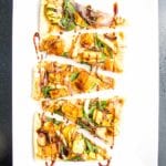 Small triangle appetizer flatbread pizza slices loaded with hummus, spinach, roasted squash, onions and garlic with a date syrup drizzle