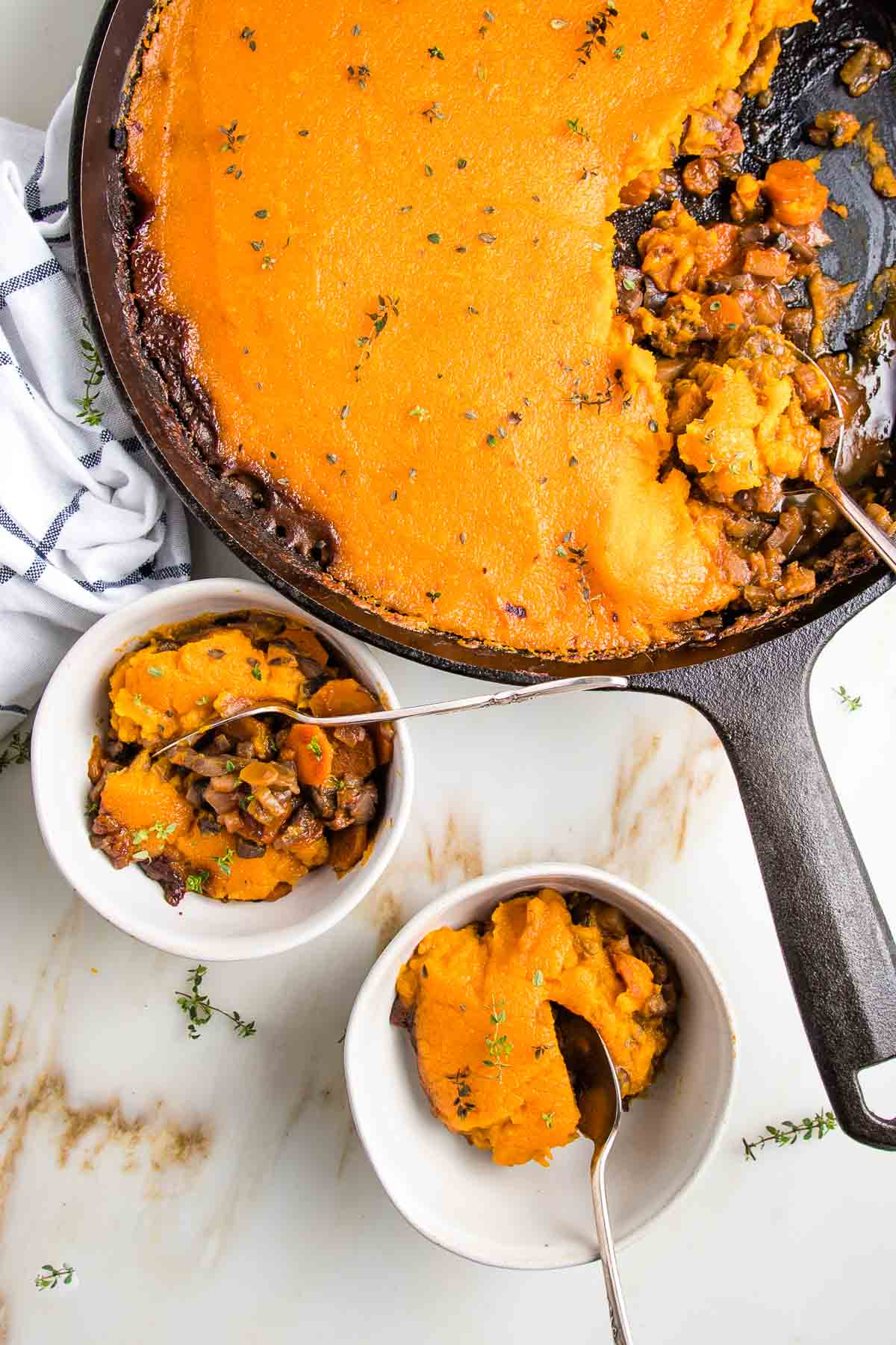 Cast iron skillet filled with lentil shepherds pie topped with sweet potato mash. Two small bowls with servings of vegan shepherd's pie on the bottom left of photo.