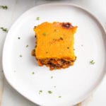 White rimmed plate with a square of veggie shepherd's pie, topped with sweet potato mash, sprinkled with fresh thyme.