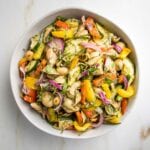 White bowl filled with pasta salad loaded with colorful vegetables and small shells with pesto sauce and fresh slivers of basil.