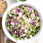 White bowl filled with colorful chopped salad and an orange dressing, plus sunflower seeds. There is a small white bowl with same orange chipotle dressing on the side.