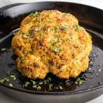 Golden brown whole roasted cauliflower, sprinkled with fresh herbs.