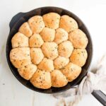 Cast iron skillet filled with round herby dinner rolls.