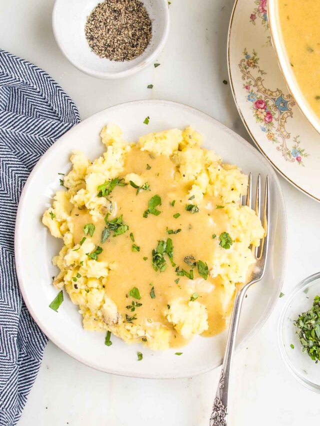 Plate full of mashed potatoes covered in gravy and sprinkled with fresh herbs.