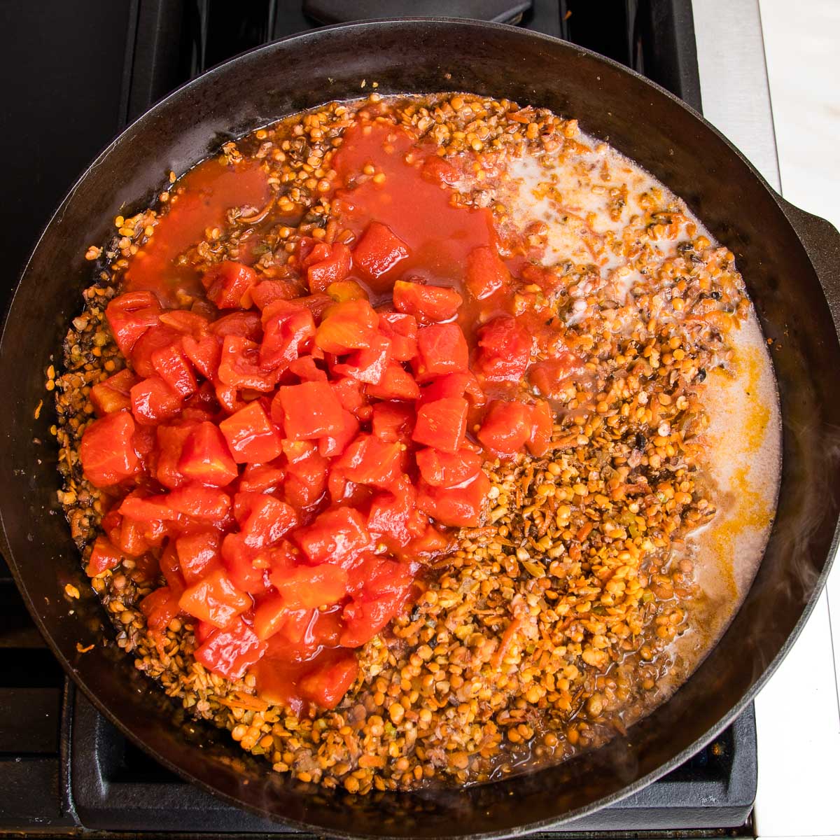 Diced tomatoes, almond milk and tamari are added to a cast iron pot filled with sauteed veggies.