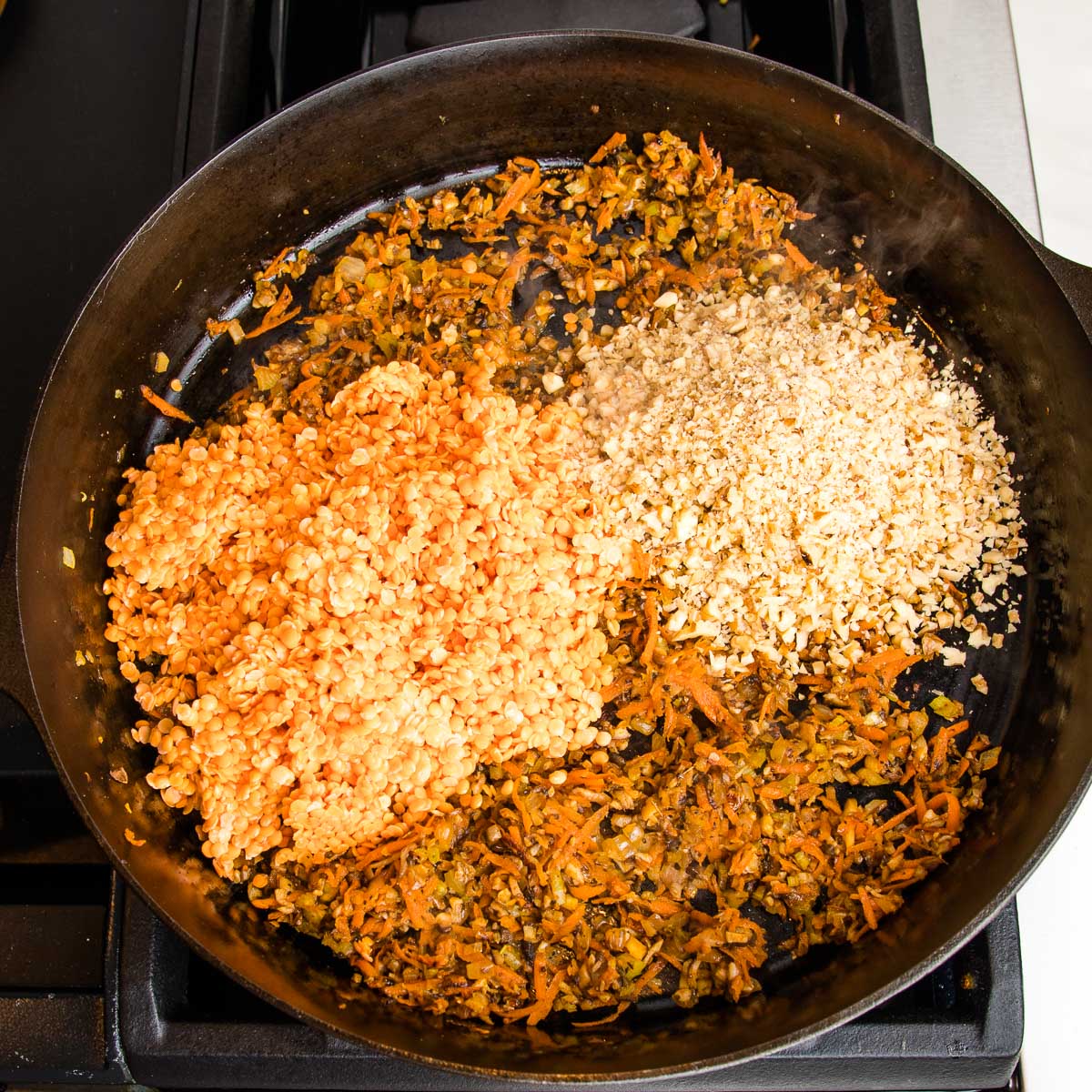 Red lentils and finely chopped walnuts are added to a cast iron pan that is filled with sauteed mushrooms, carrots, celery, onions and spices.
