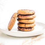 Stack of cookies with some melted chocolate sprinkles and one leaning against the stack.