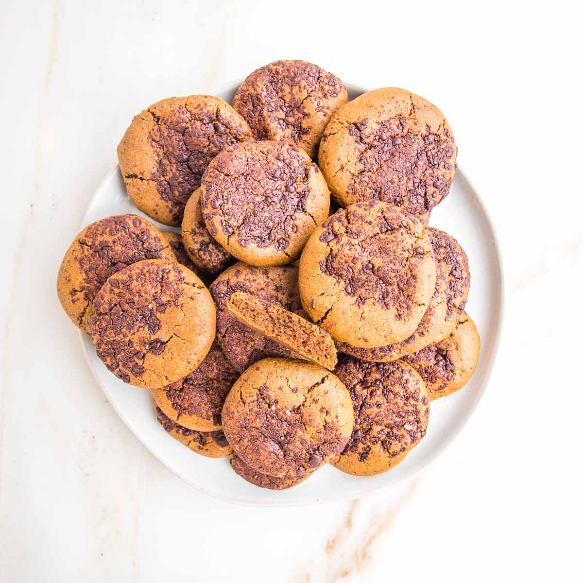 Plate filled with ginger crinkle cookies, topped with chocolate. One cookie is broken open to see the chewy center.