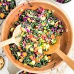 wooden salad bowl filled with colorful chopped salad: tuscan kale, purple carrots, red peppers, purple cabbage, cucumbers and marcona almonds