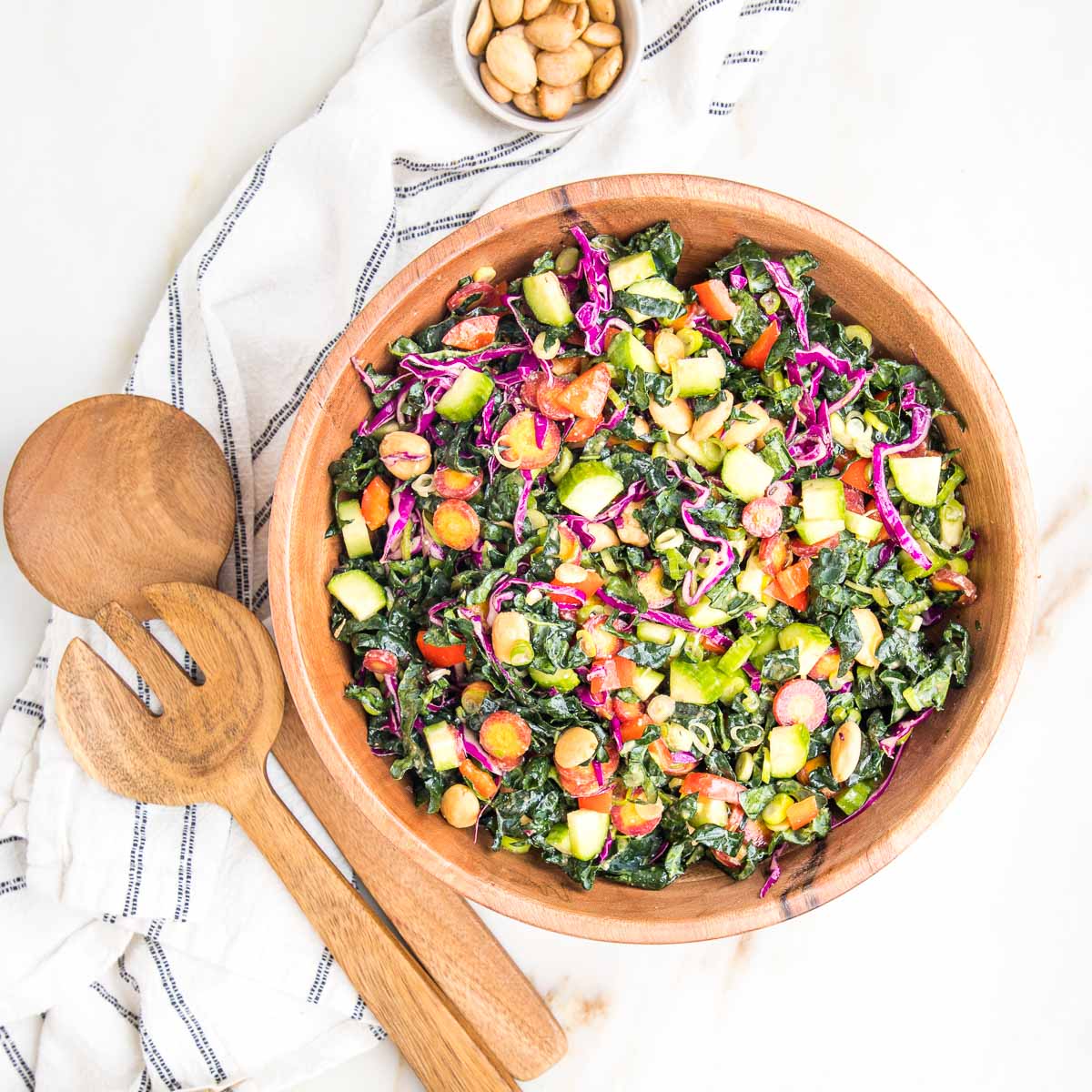 Colorful chopped salad in a wooden bowl with wooden salad tossers on the side and a bowl of marcona almonds. 