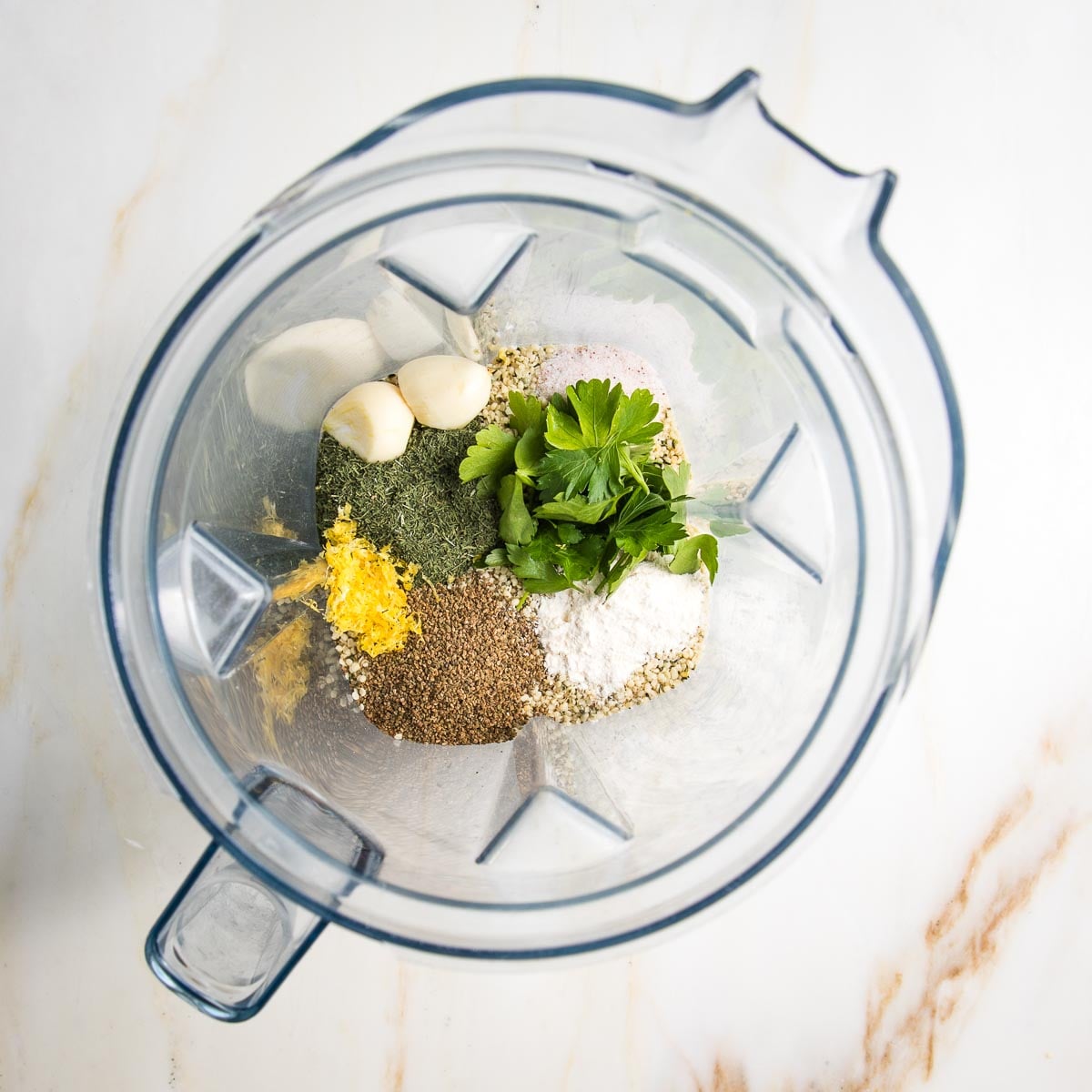 Healthy ranch dressing ingredients in a blender: you can see the lemon zest, parsley, garlic, celery seed, dill and hemp seeds.