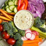Vegan ranch in a small bowl in the center of the photo, surrounded by colorful but up veggies.