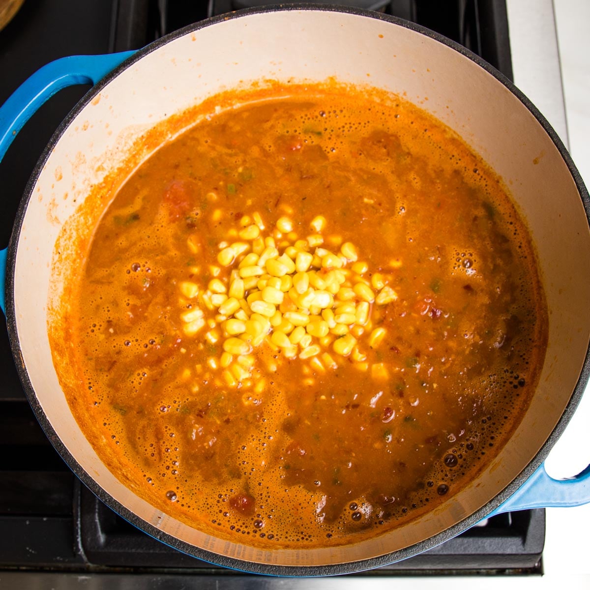 Dutch oven filled with simmering taco soup and corn has just been added to the center of pot.