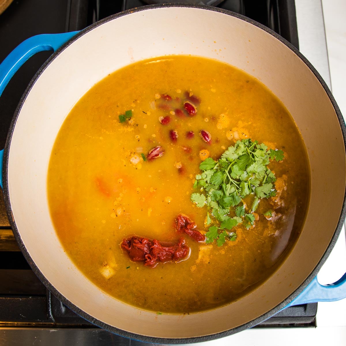 dutch oven filled with broth, tomato paste, beans, fresh cilantro.