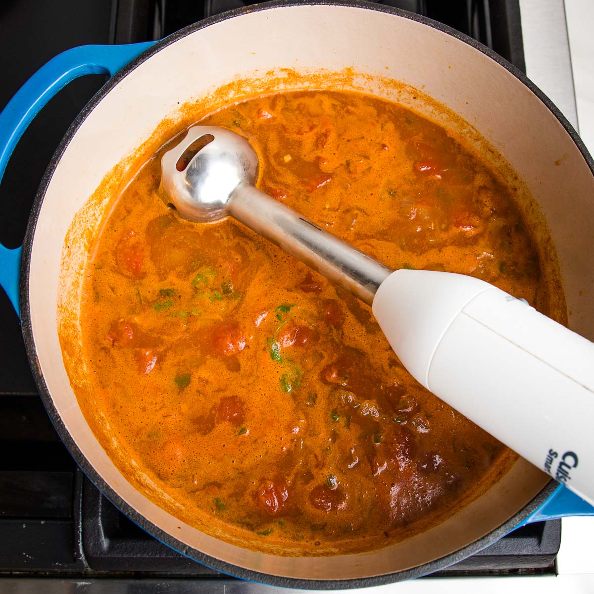 immersion blender inside a dutch oven filled with taco soup. You can see chunks of tomato, red kidney beans and fresh cilanto.