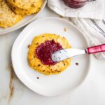 White plate with a cauliflower bun, being spread with raspberry jam.
