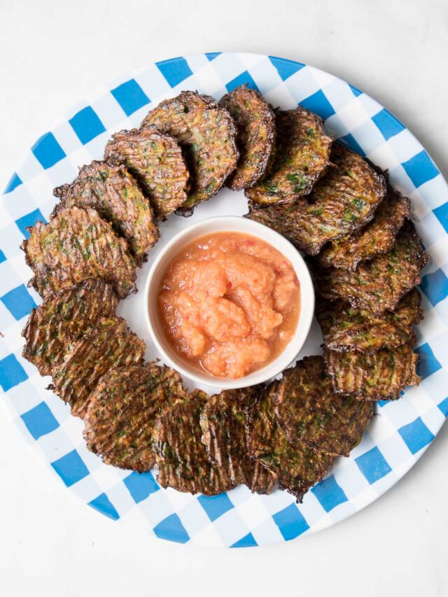 Crispy latkes in a circle around a dish of pink applesauce.