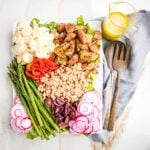 Plattered nicoise salad with sections of roasted potatoes, red peppers, small white beans, asparagus, olives, radish and hearts of palm with a side of lemon vinaigrette.