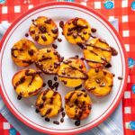 Plate of grilled peaches with a chocolate balsamic drizzle on a white and red checkered background.