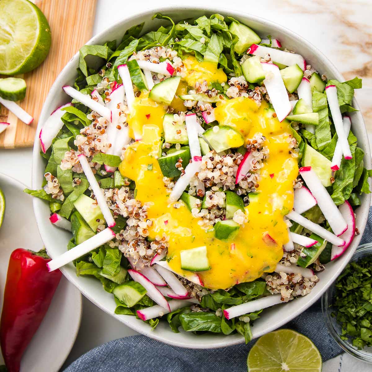Bright yellow mango dressing pouted onto a simple green and grain salad.