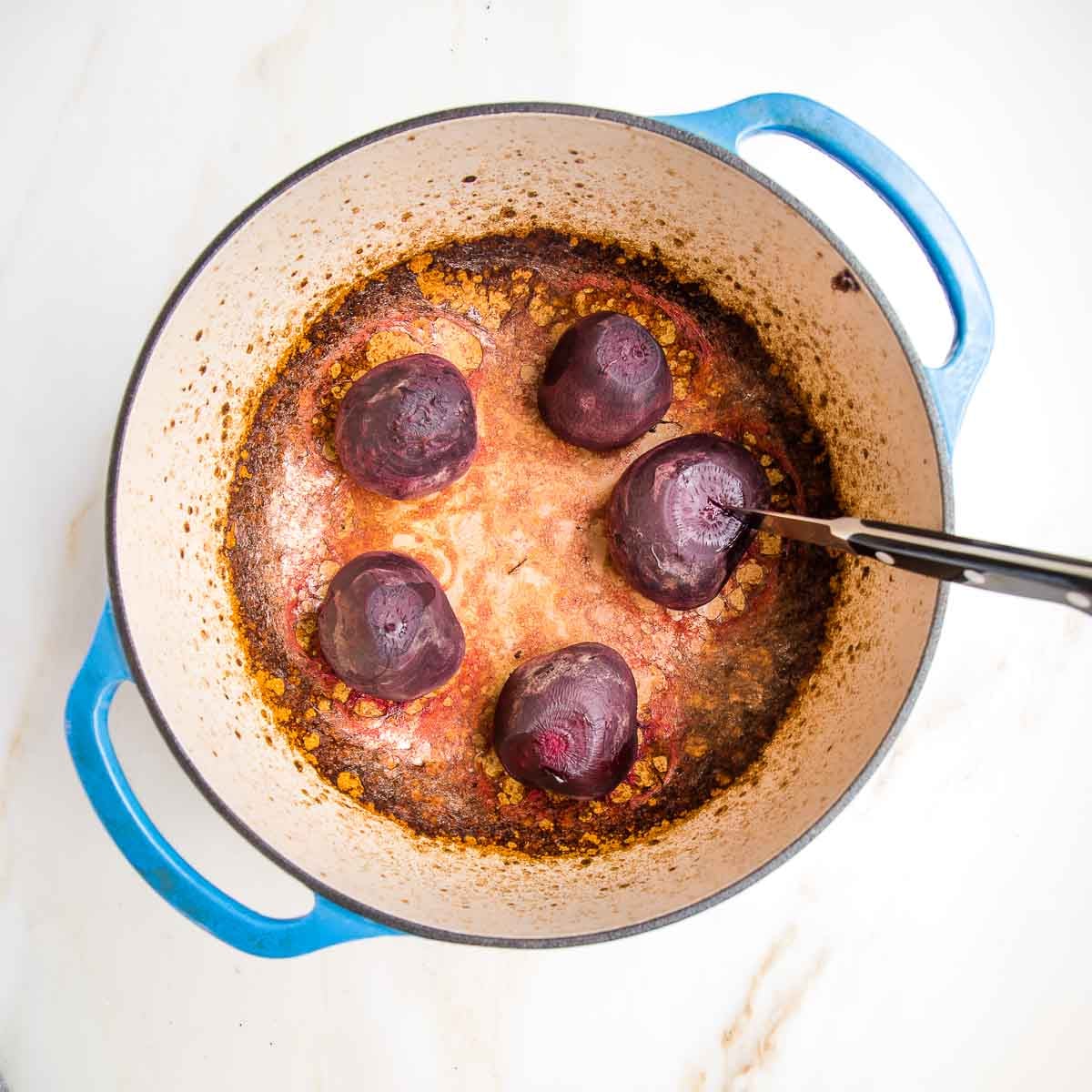 Dutch oven with cooked whole red beets inside. A small paring knife is stuck into one of the beets.
