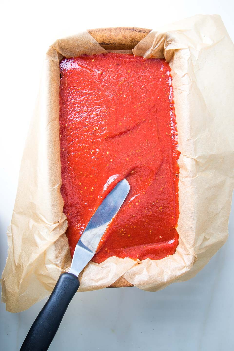 Offset spatula spreading tomato mixture onto top of vegan meatloaf.