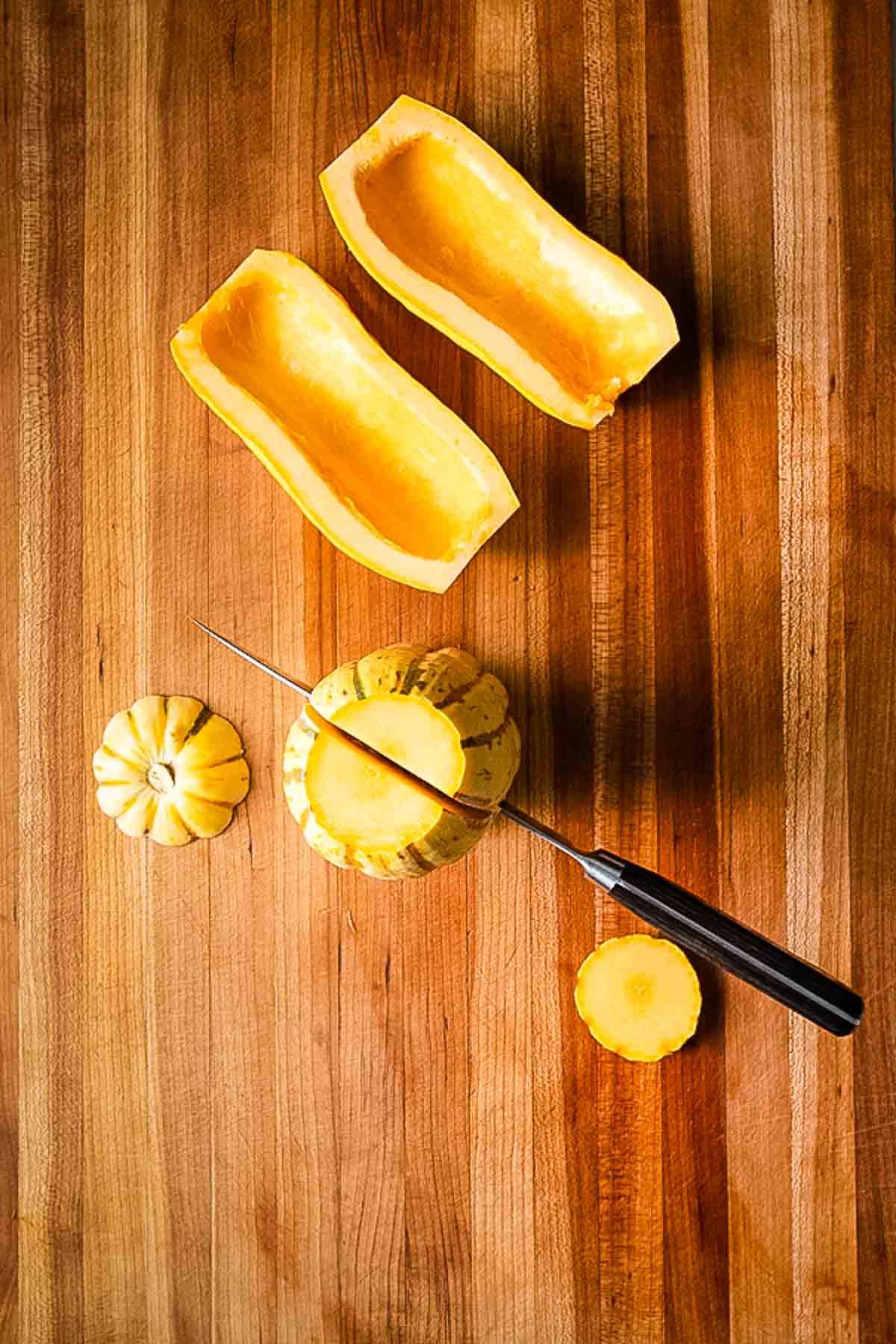 Delicata squash, halved and seeds scooped out. Another on the cutting board, showing how to slice lengthwise.