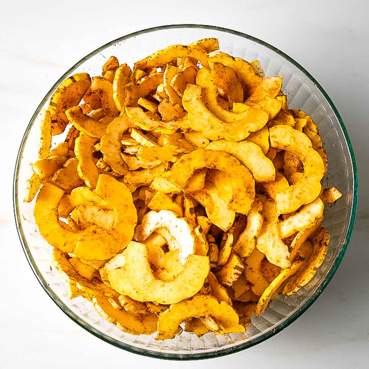 Glass bowl filled with spiced delicata half moon thin slices.